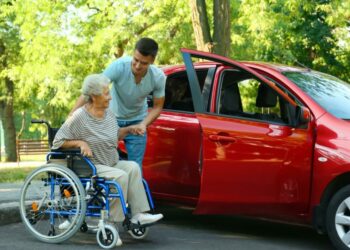 Young Man helping Old Woman into car from wheelchair