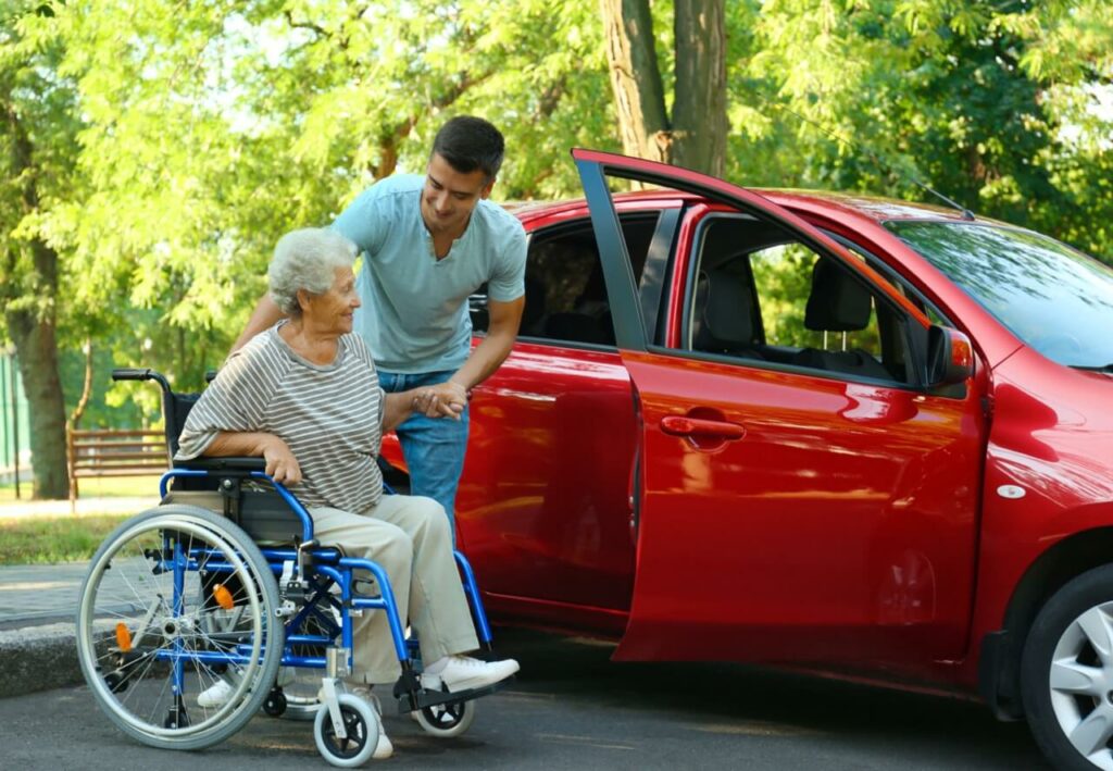 Young Man helping Old Woman into car from wheelchair