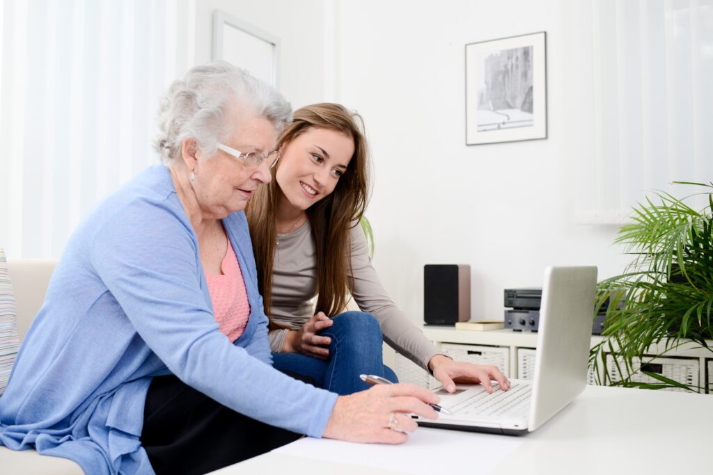 cheerful young woman teaching computer to an old senior woman at home